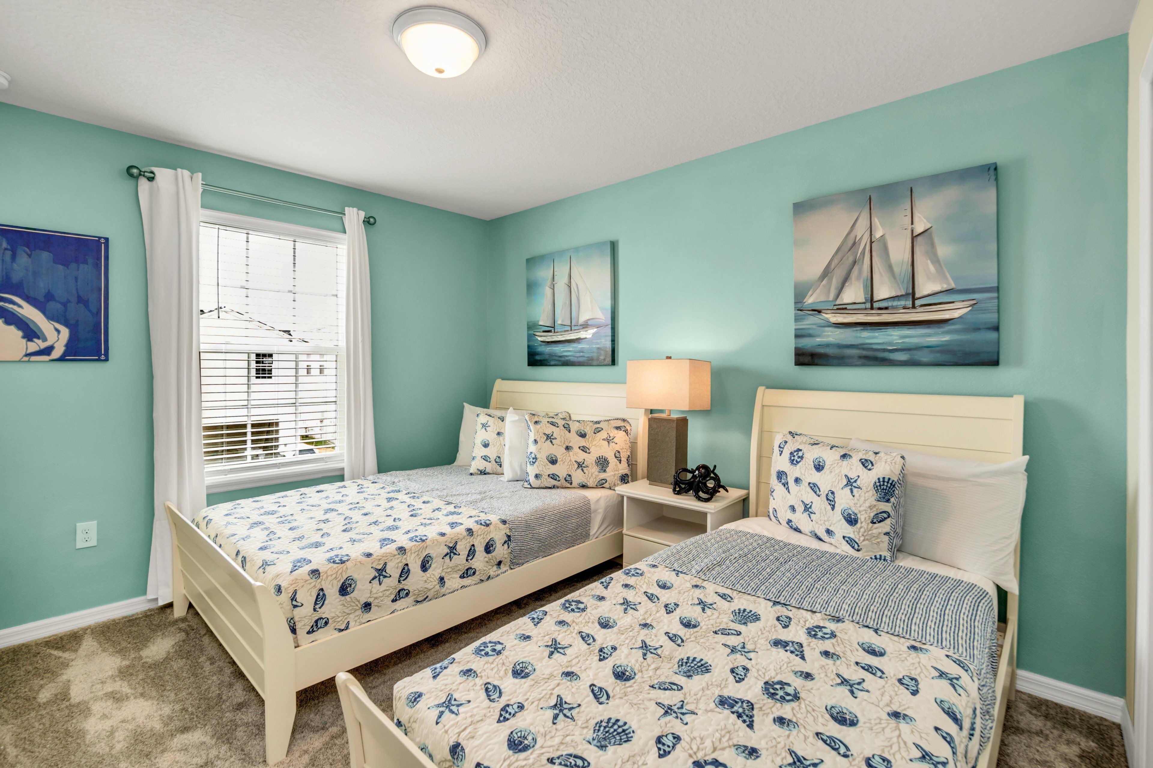 A bedroom with two beds, a window with white curtains, and nautical-themed wall art.