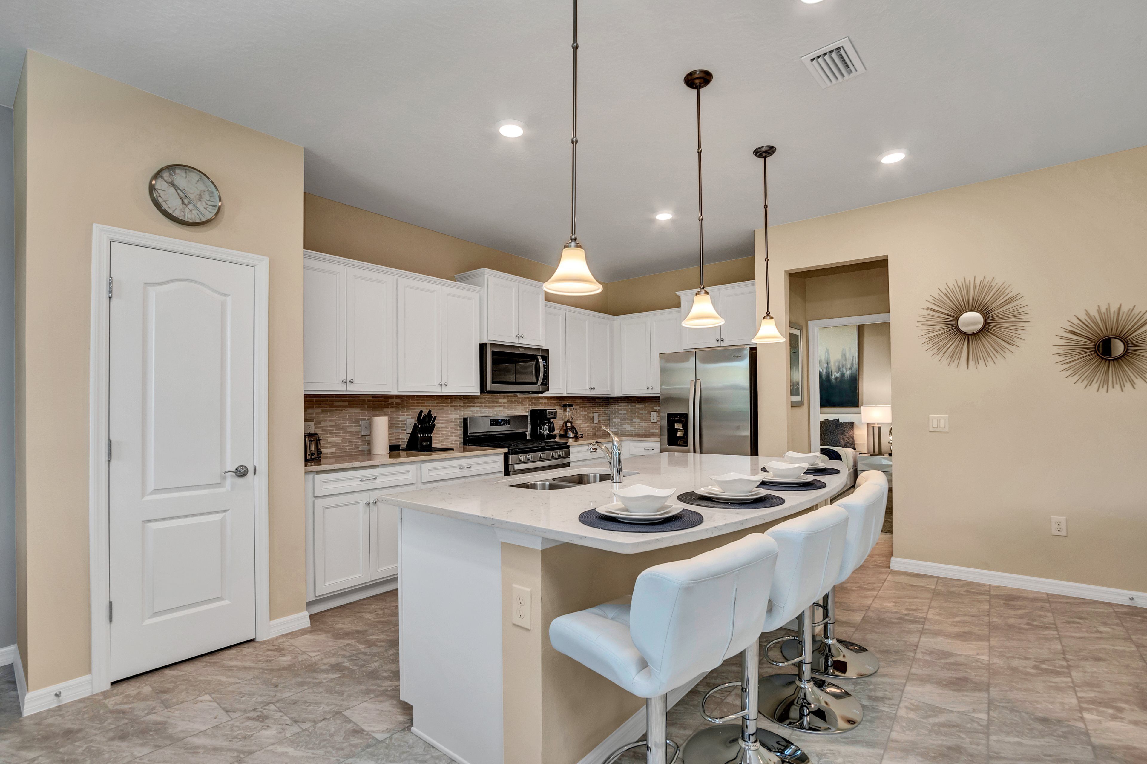 A modern kitchen with white cabinets, a central island with bar stools, stainless steel appliances, and pendant lighting.