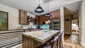 Eine moderne Küche mit Holzschränken, einer Marmorinsel und einem Edelstahlkühlschrank.