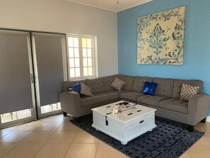 A living room with a sectional sofa, a coffee table, and a large window with blinds.