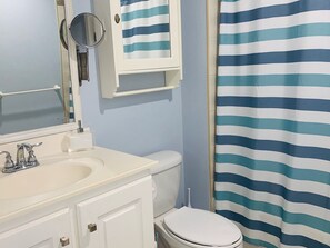 A bathroom with a white sink, a mirror, a toilet, and a striped shower curtain. - Luxury spacious condo in the heart of it all (Barbados)