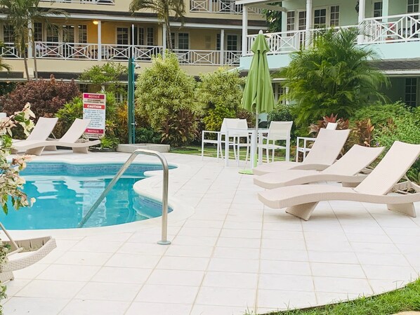 A pool area with lounge chairs and a sign. - Luxury spacious condo in the heart of it all (Barbados)