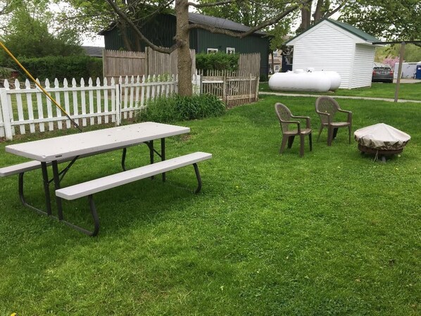 A picnic setup with a table and benches in a grassy backyard, surrounded by a white picket fence and a small shed. - Lake Ontario 2 bedroom/2 bath - between Rochester and Niagara Falls (Kent)