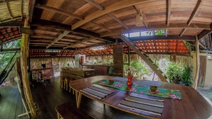 A wooden dining area with a round table, benches, and a thatched roof structure. - Curuá House (Alter do Chão)
