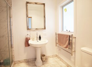 A bathroom with a pedestal sink, a mirror with an ornate frame, a towel rack, and a window. - Bridgecroft Villa (Richmond)