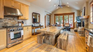 A spacious kitchen with a large island, wooden cabinets, a stone backsplash, and a stone fireplace.