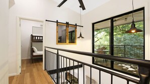 Un interior moderno con una escalera de madera, barandilla negra, zona de comedor con vista a zonas verdes y un espejo con marco negro.