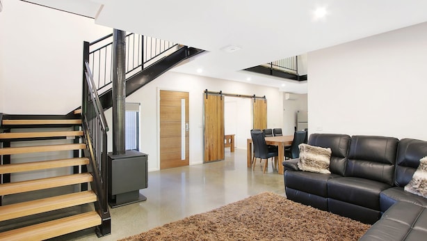Un interior moderno con una escalera, un sofá de cuero negro, un comedor y una puerta de madera.