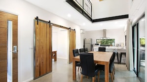 Una cocina moderna con un ventanal grande, un comedor con mesa y sillas de madera, y una puerta corredera de madera.