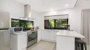 Una cocina moderna con armarios blancos, horno empotrado, microondas y un amplio ventanal con vistas a árboles.