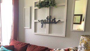 A living room with a red sofa, a floral throw blanket, a 'gather' sign, and a mirror on the wall.