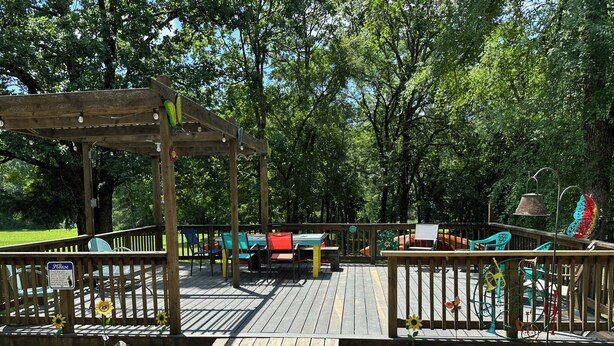 A wooden deck with a pergola, outdoor seating, and a playground area with colorful chairs and a slide.