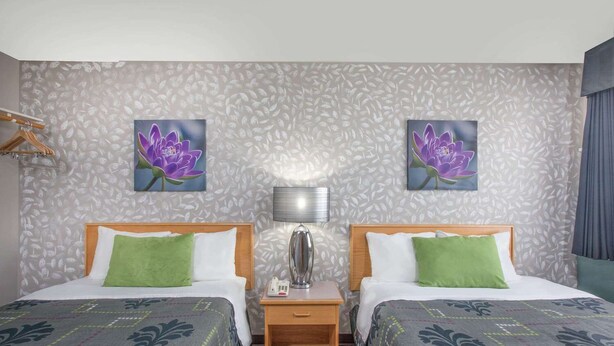 Ein Hotelzimmer mit zwei Betten, einem Nachttisch, einer Lampe und zwei floralen Bildern an der Wand.