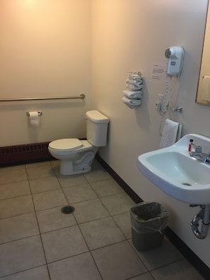 A standard bathroom with a toilet, sink, hand dryer, and a trash can.