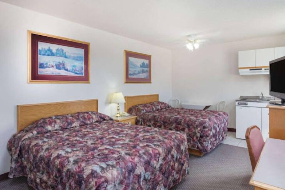 A hotel room with two beds, a desk, a chair, and a kitchenette.