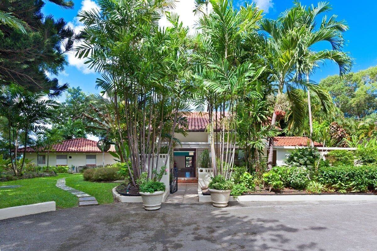 Un complexe hôtelier tropical doté d’une allée dallée, de palmiers et d’un bâtiment à toiture rouge.