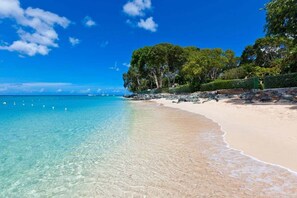 Ein Strand mit klarem türkisblauem Wasser, einem Sandufer und Bäumen im Hintergrund.