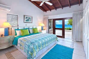 A bedroom with a bed, two nightstands, a ceiling fan, a window with blinds, a view of the ocean, and a sliding glass door. - Church Point 4 by Blue Sky Luxury (Holetown)