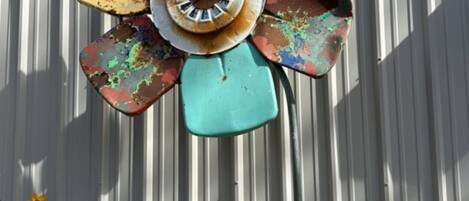 A rusted, colorful fan-shaped object mounted on a pole, with a 'hello' sign and a watermelon sign nearby.