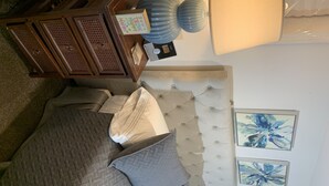 A bedroom with a tufted headboard, a bed with multiple pillows, a wooden dresser, and two abstract paintings on the wall. - 1 bedroom apt.Minutes to Encore Casino and Boston. (Revere)