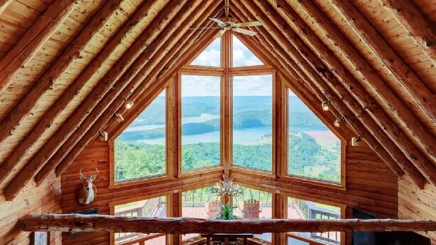 Una baita di legno con tetto a punta e ampie finestre che si affacciano su un lago e una foresta.