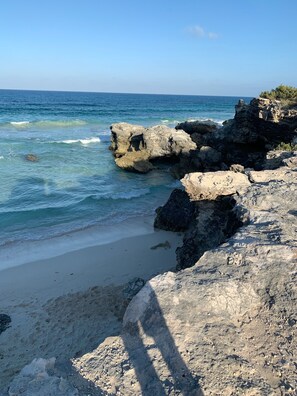 Una costa rocosa con agua azul cristalina y una playa arenosa.