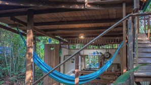 Una cabaña de madera con una hamaca, una terraza de madera y un interior rústico.