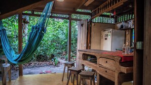 Una habitación rústica de madera con una hamaca, un escritorio de madera, taburetes y un refrigerador.