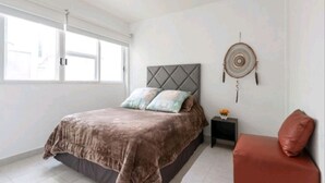 A bedroom with a bed, a nightstand, a red chair, and a wall decoration.