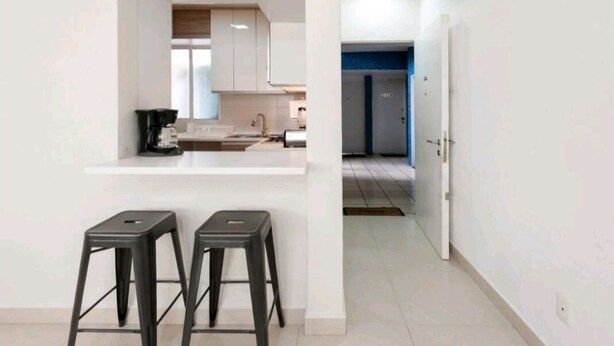 A modern kitchen with white cabinets, a coffee machine, and two black stools.