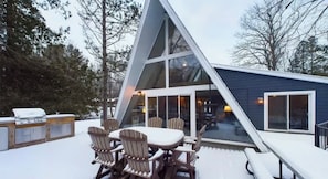 A modern A-frame cabin with a deck, outdoor seating, and a barbecue area.