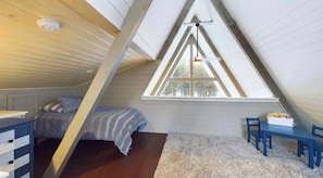 A bedroom with a sloped ceiling, a bed, a desk, and a window.