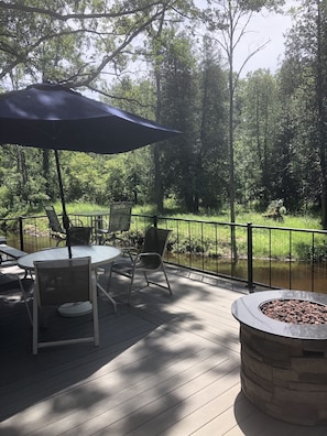 Relax by the water's edge, surrounded by lush greenery, with a fire pit and comfortable seating.