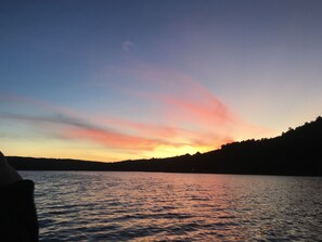 A sunset over a calm lake with a silhouette of a forested hill in the background. - Adirondack Escape on the Great Sacandaga Lake (Hadley)