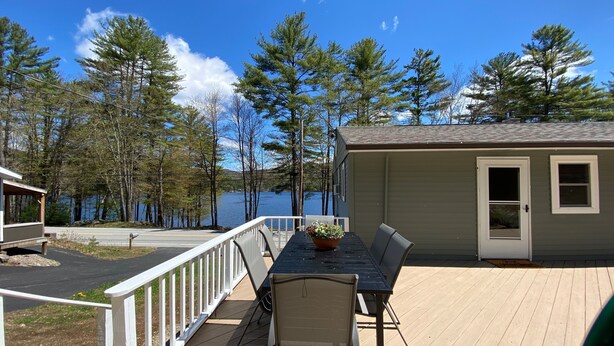 A deck with a table and chairs, overlooking a lake with trees and a small building. - Adirondack Escape on the Great Sacandaga Lake (Hadley)
