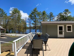 A deck with a table and chairs, overlooking a lake with trees and a small building. - Adirondack Escape on the Great Sacandaga Lake (Hadley)