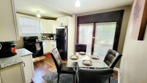 Cocina compacta con armarios blancos, un refrigerador negro y un comedor con mesa lista para dos.
