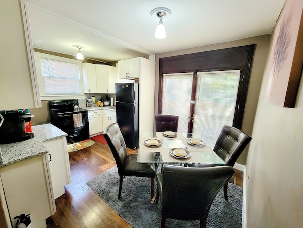 A compact kitchen with white cabinets, a black refrigerator, and a dining area with a table set for two.