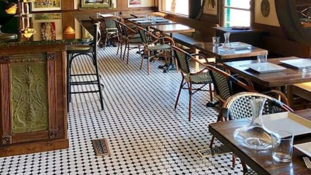 Un restaurante con suelo estampado, mesas y sillas de madera y un techo con diseño geométrico.