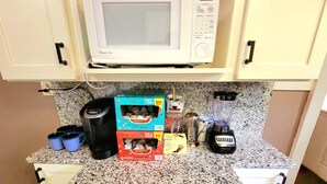 Una cocina con microondas, cafetera, licuadora y diversos utensilios sobre la encimera.