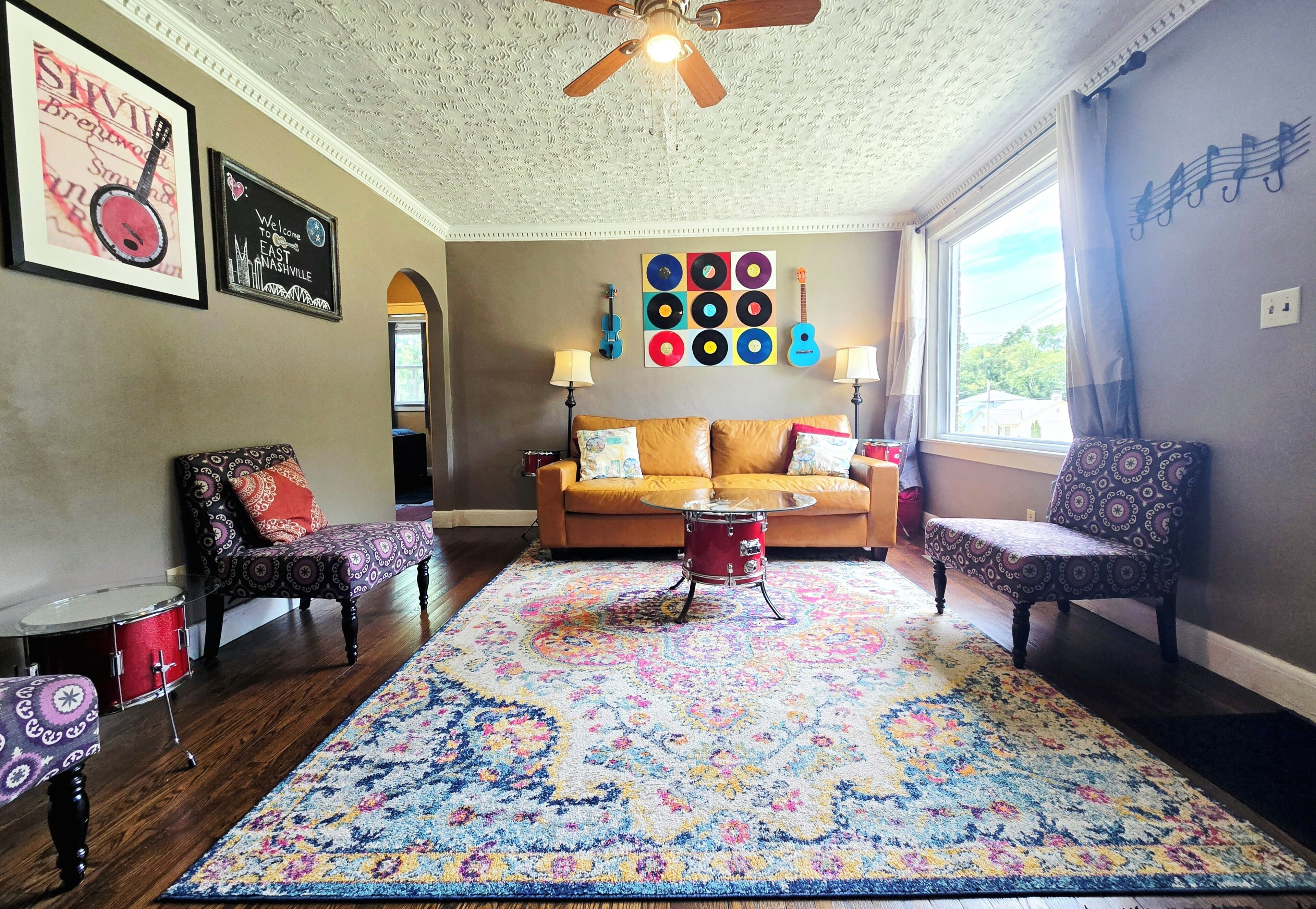A living room with a patterned rug, a red drum set, a sofa, and a wall with vinyl records.