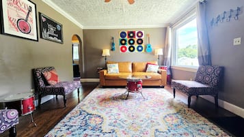 A living room with a patterned rug, a red drum set, a sofa, and a wall with vinyl records.