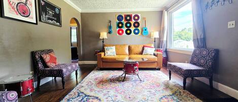 A living room with a patterned rug, a red drum set, a sofa, and a wall with vinyl records.
