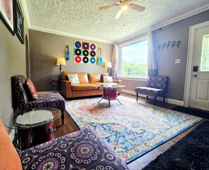 A living room with a patterned rug, a drum set, a sofa, and a wall with a record collection.