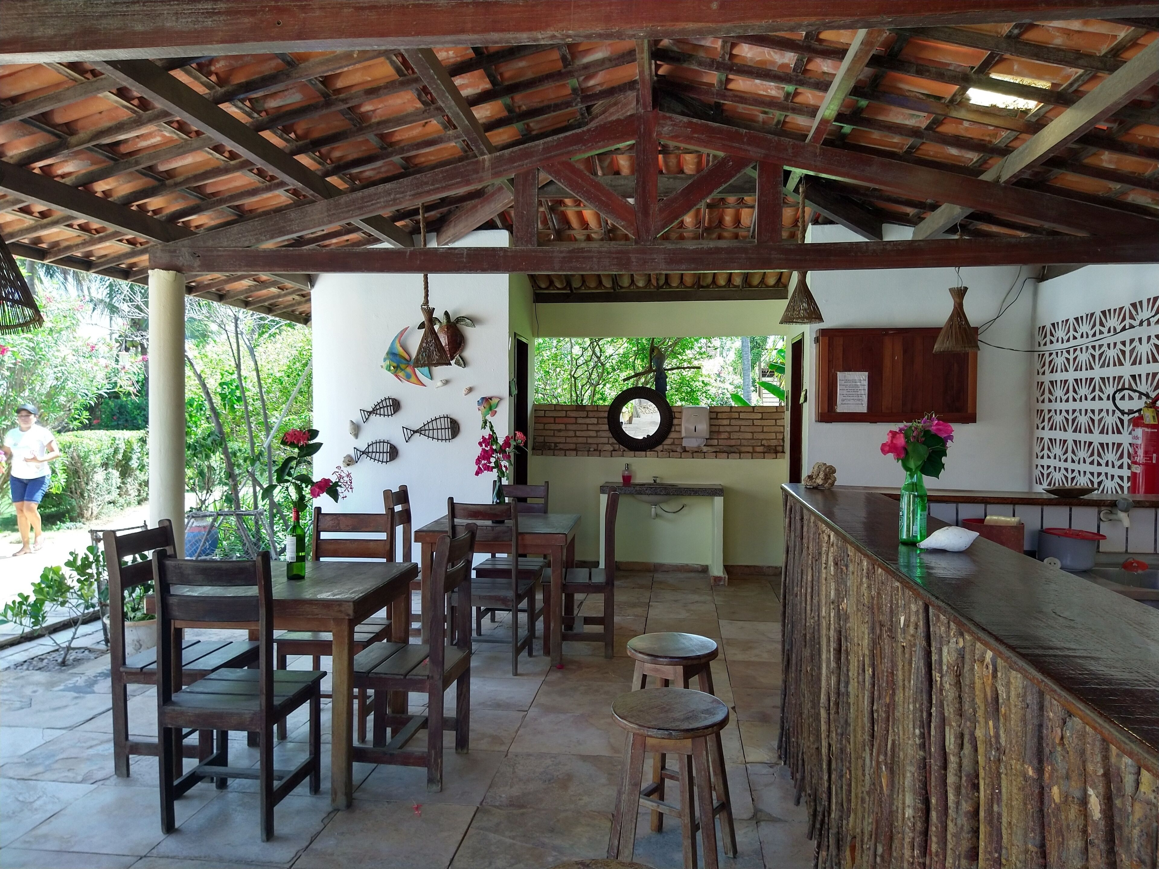 An outdoor dining area with wooden tables and chairs, a bar counter, and a rustic ceiling.