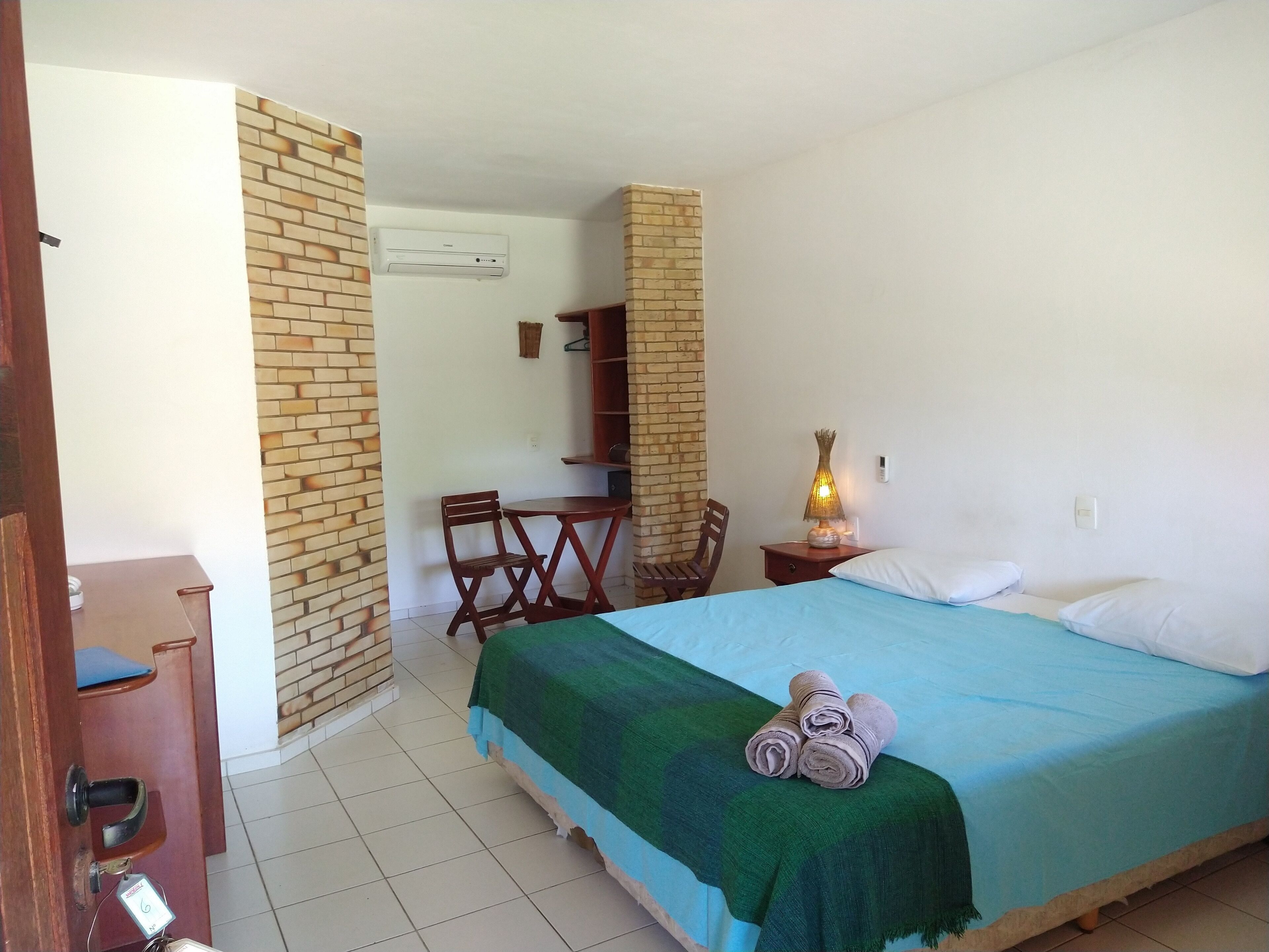 A bedroom with a bed, a chair, a small table with a lamp, and a brick-patterned wall.
