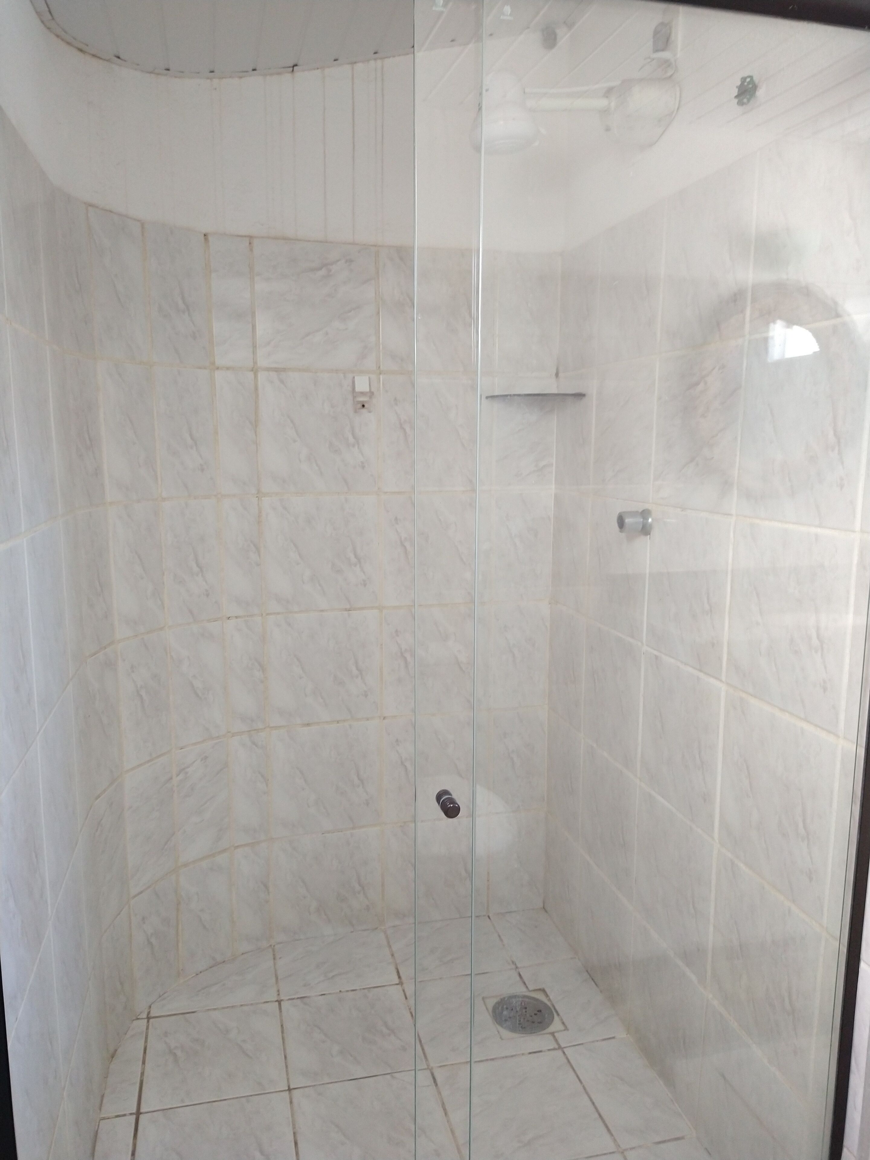 Une douche fermée par des parois de verre, avec des carreaux de marbre blanc et un drain au centre.