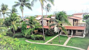 A residential area with multiple houses, each featuring a red-tiled roof and surrounded by lush greenery, including palm trees and well-maintained gardens.