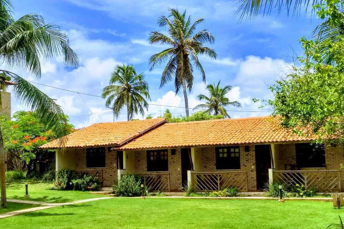 A two-story brick building with a tiled roof, surrounded by a well-maintained lawn and palm trees.