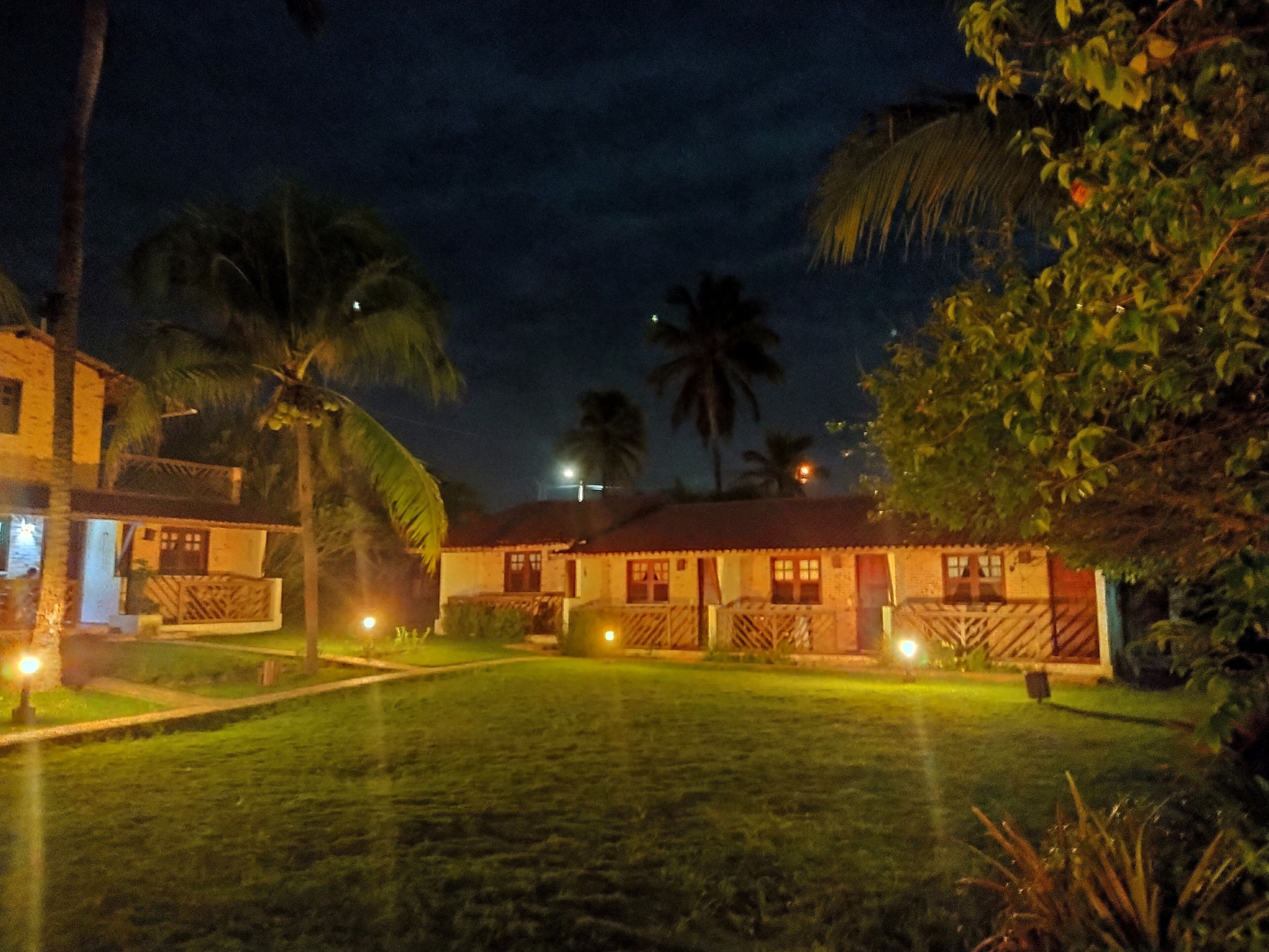 A nighttime view of a bungalow-style hotel with a well-lit lawn and palm trees.